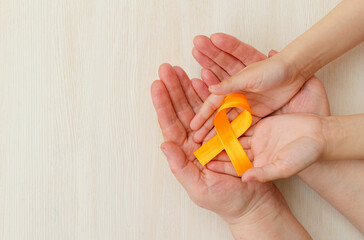 Hands of mother and child hold orange ribbon on white background.Concept. World Multiple Sclerosis day.Layout. Copy space. Banner. Mock up.close up.