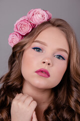 portrait of pretty brunette girl with pink roses in her hair on gray background. flowers in curls on the head. spring, flowering, colors. fashion photo