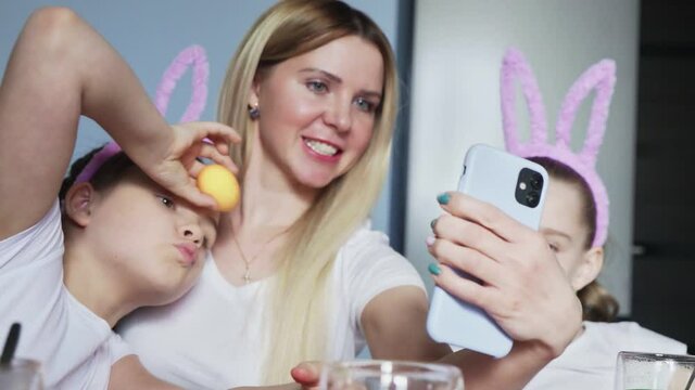 Happy family preparing for Easter. Cute little girls with mother wearing bunny ears takes selfie photo on Easter day.