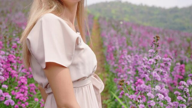 A carefree blonde hair girl slowly dancing inside a blooming purple flower field, attractive young woman feeling free turning around in spring garden in summer day, woman touching nature, body care