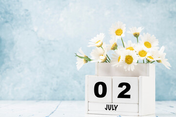 cube calendar for July with daisy flowers over blue