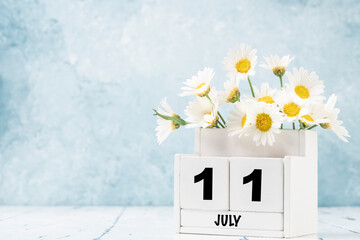 cube calendar for July with daisy flowers over blue