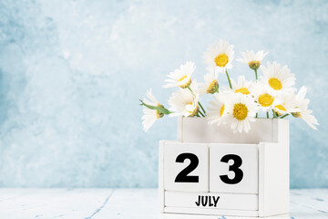 cube calendar for July with daisy flowers over blue