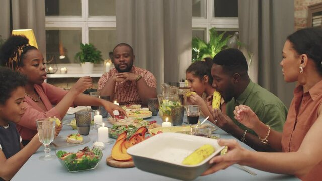 Medium PAN Shot Of Big Joyful Afro-american Family Having Dinner At Home Together, Chatting And Exchanging Plates Having Good Time Celebrating Special Occasion