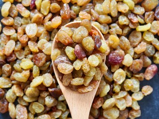 Wooden spoon with raisins on black background. Close-up. Place for text
