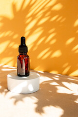 A cosmetic bottle with an amber glass dropper sits on a concrete pedestal. Natural beauty products. Mineral organic oil. Empty bottle for skin care. Hard sunlight.