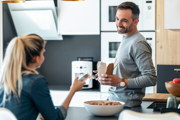 Funny cute couple eating and taking photos with smartphone in the kitchen at home.