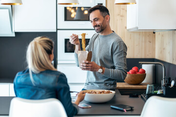 Funny cute couple eating and taking photos with smartphone in the kitchen at home.