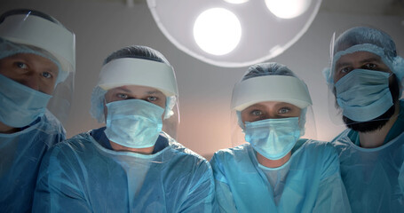 Fototapeta na wymiar Low angle view of team of surgeons in protective mask and face shield looking at camera
