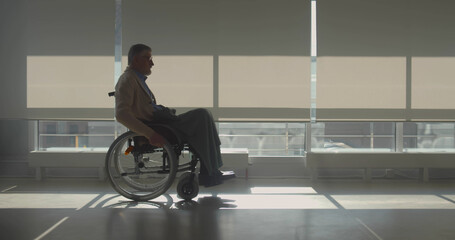 Side view of senior man in wheelchair riding at hospital corridor