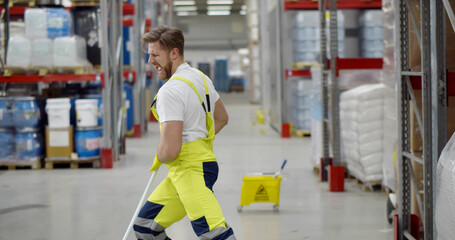 Funny male janitor dancing with mop in warehouse