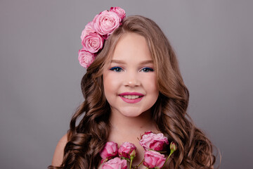 brunette teenage girl with pink roses in her hair on gray background. flowers in curls on the head. fashion photo