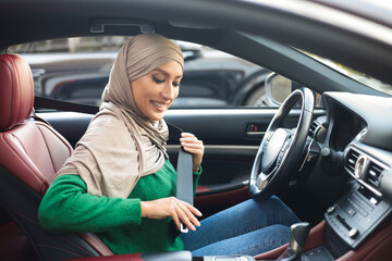 Fototapeta na wymiar Smiling Muslim Woman In Hijab Putting On Seat Belt