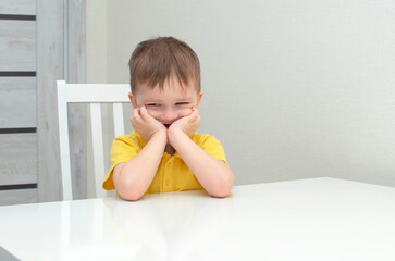 Portrait of a cute four-year-old child in a yellow shirt sitting at a table. Happy boy, smile.