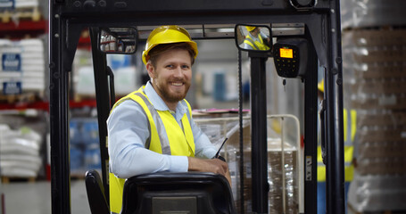 Portrait young male warehouse worker sitting in forklift truck and smiling at camera © TommyStockProject