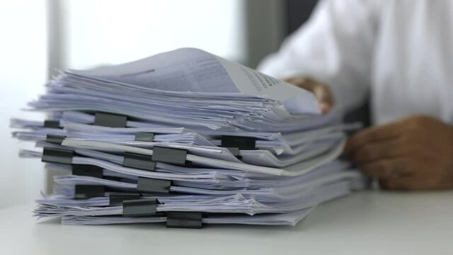A young business man in a suit is managing paperwork in the office. Many paperwork that is not finished. Documents in the company about finance and information of the company.