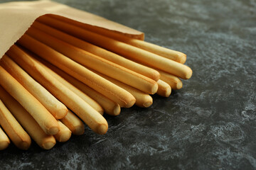 Paper bag with grissini breadsticks on black smoky background