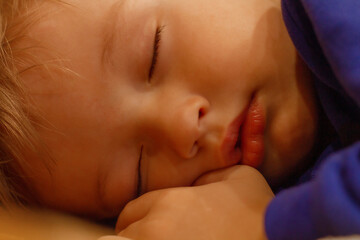 a small sleeping handsome boy blond with plump lips  in a blue jacket