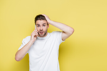 shocked man touching head during conversation on cellphone on yellow