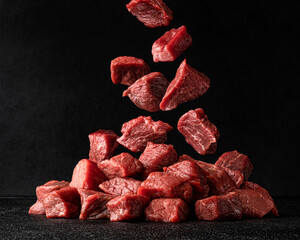 Cubes of raw beef falling over black background