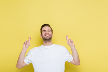 cheerful man with closed eyes standing with crossed fingers on yellow