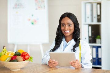 Young black nutritionist with touch pad creating plant based meal plan for client at clinic, blank space