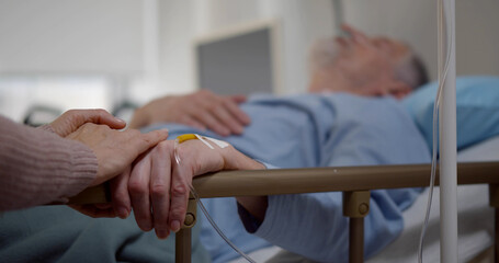 Sick senior man in hospital bed and his wife sitting next to him