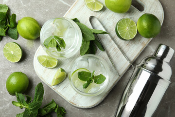 Board with glasses of mojito cocktail and ingredients on gray textured table