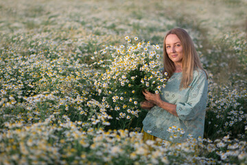 Beautiful girl with long blond hair and a beautiful slack in a chamomile field with a bouquet of...