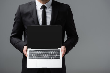 cropped view of businessman holding laptop with blank screen isolated on grey