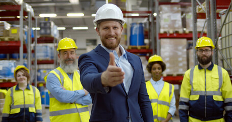 Smiling warehouse owner stretching hand for handshake with team standing on background
