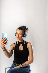 Alternative girl with tattoo using her cell phone and wireless headphones wearing a sleeveless top. Person in a video meeting.