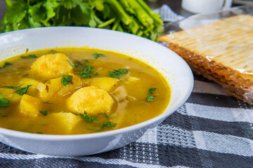 Delicious matzo ball or kneidlach soup. Jewish traditional cuisine, homemade gluten free version. Hot and comforting matzah ball soup with vegetables. Matzos, celery and coriander in background.