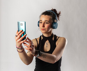 Alternative girl with tattoo using her cell phone and wireless headphones wearing a sleeveless top. Person in a video meeting.