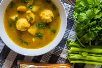 Matzo ball or kneidlach soup. Jewish traditional cuisine, homemade gluten free version. Hot and comforting matzah ball soup with vegetables. Matzos, celery and coriander in background. Top view