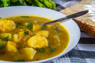 Delicious matzo ball or kneidlach soup and a spoon. Jewish traditional cuisine, homemade gluten free version. Hot and comforting matzah ball soup with vegetables. Matzos and celery in background.