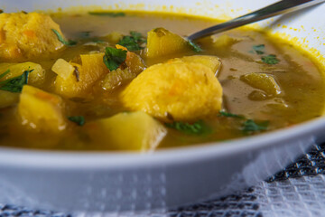 Delicious matzo ball or kneidlach soup and a spoon. Jewish traditional cuisine, homemade gluten free version. Hot and comforting matzah ball soup with vegetables. Matzos in background. Closeup