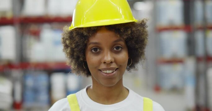 Portrait of african woman worker in safety hardhat standing in warehouse