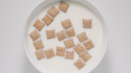 Breakfast cereal bites in a milk in a white bowl, top view