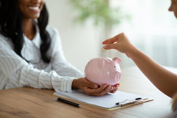 Obraz na płótnie Canvas Financial planning concept. Closeup of business women putting coin into piggy bank at modern office