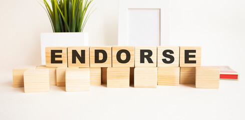 Wooden cubes with letters on a white table. The word is ENDORSE. White background.