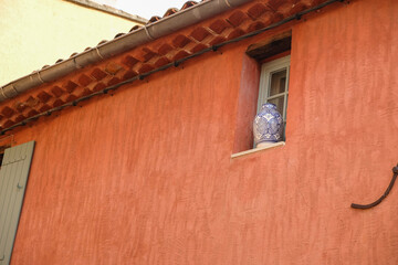 Red ocher wall of an old house. The window is decorated with a large white vase with blue ornaments. Mass production vase. Copy space. 
