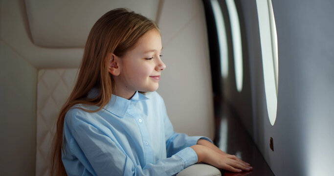 Child sitting in airplane seat and looking at window.