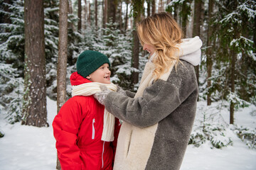 A young mother adjusts her son's scarf on a frosty morning in the woods