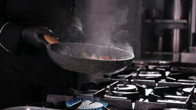 Close-up of a chef working the frying pan for roasting mixed colorful vegetables, tossing and turning them in the air, restaurant kitchen , slow motion