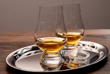 Tasting glasses of single malt scotch whisky served on steel mirror tray with reflection