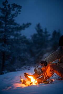 Man sitting in a snow-clad forest pouring coffee made on woodfire into a wooden cup.