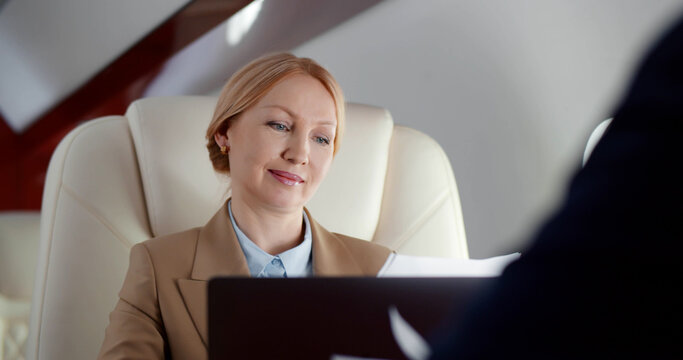Close up of mature businesswoman reading contract and discussing with partner flying in first class