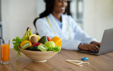 Nutritionist working on laptop, giving online consultation to client at clinic, focus on bowl of...