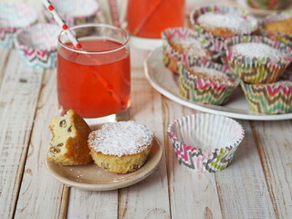 Freshly baked homemade raisin muffins in paper tins on a wooden background with raspberry juice.